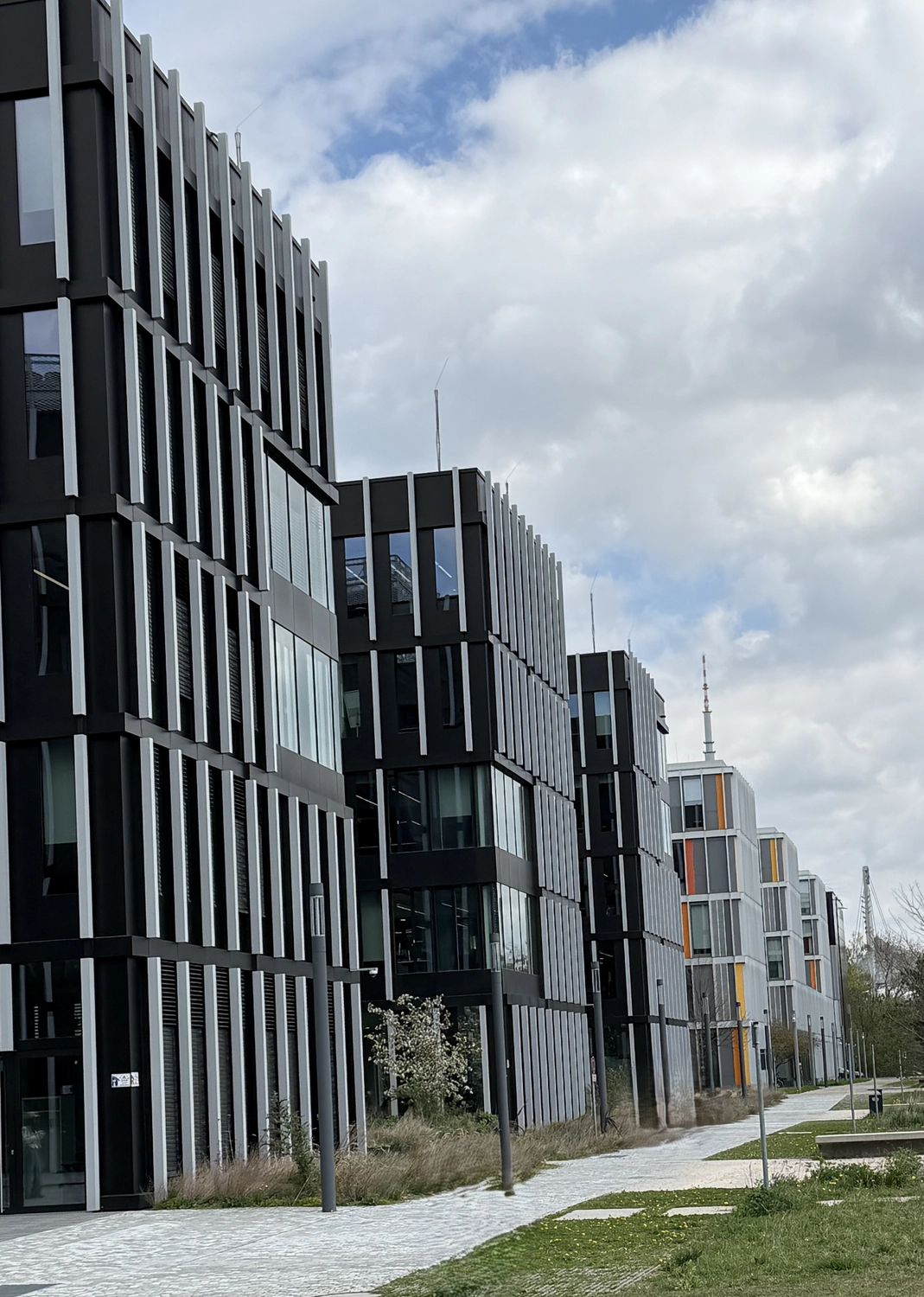 Planungsbüro Fiertel – Sicherheitstechnik – Das Qubes-Gebäude auf dem Münchner Technologiecampus mit seiner dunklen Fassade und den markanten vertikalen weißen Elementen - Brandschutzkonzept Neufarn